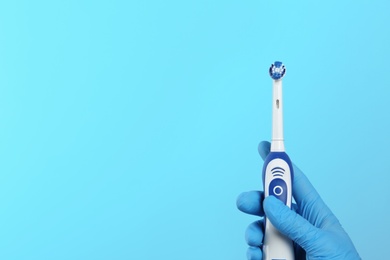 Dentist holding electric toothbrush on color background, space for text