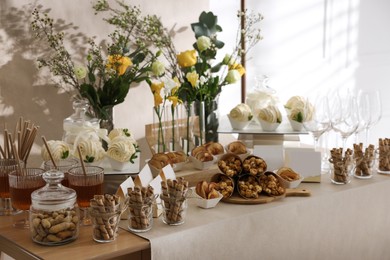 Photo of Delicious treats and glasses of drink on wooden table in room. Sweet buffet