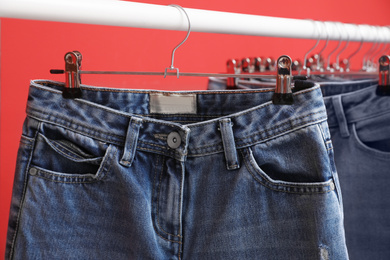 Rack with stylish jeans on red background, closeup