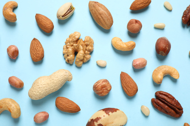 Different delicious nuts on light blue background, flat lay