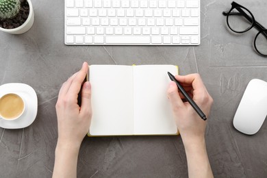 Photo of Woman writing in notebook at grey table, top view