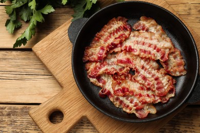 Delicious bacon slices in frying pan on wooden table, top view