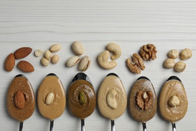 Photo of Tasty nut butters in spoons and raw nuts on white wooden table, flat lay. Space for text