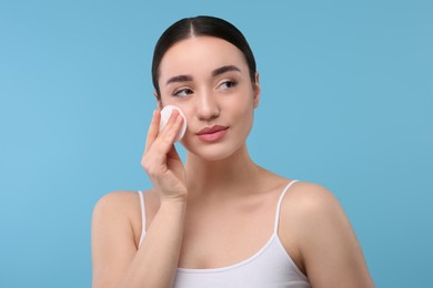 Photo of Beautiful woman removing makeup with cotton pad on light blue background