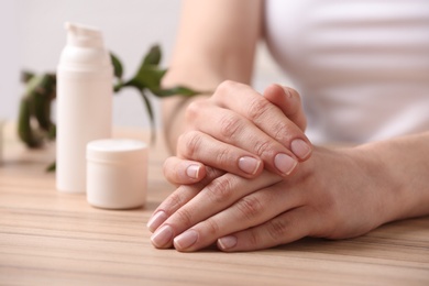 Young woman showing hands with smooth skin at wooden table, closeup