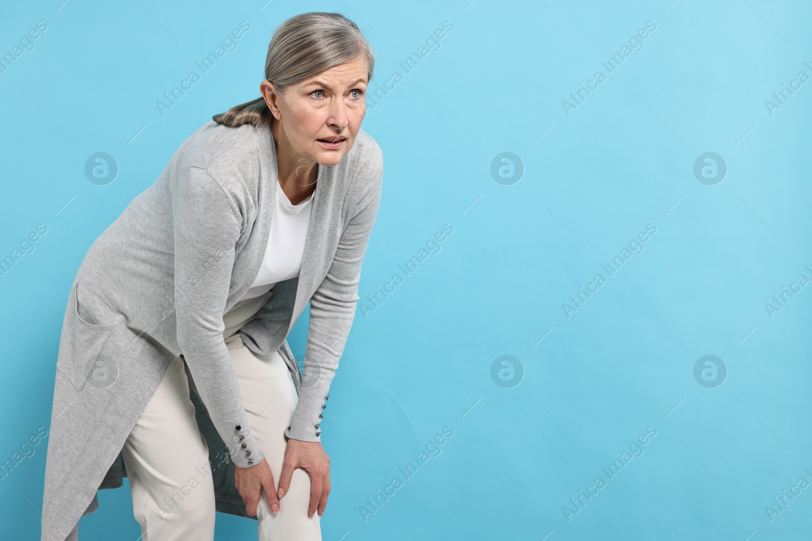 Photo of Arthritis symptoms. Woman suffering from pain in knee on light blue background, space for text
