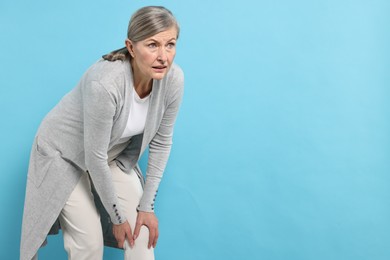 Photo of Arthritis symptoms. Woman suffering from pain in knee on light blue background, space for text
