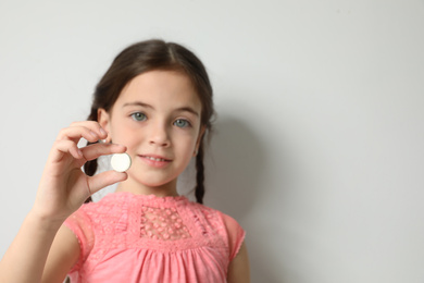Photo of Little girl with vitamin pill against light background, focus on hand. Space for text