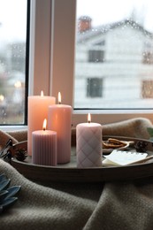 Photo of Tray with burning wax candles and decor on window sill indoors