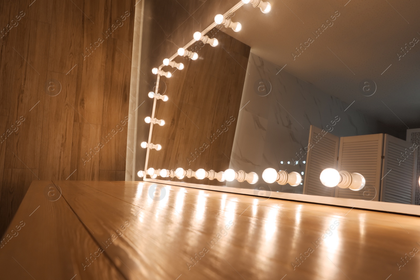 Photo of Modern mirror with light bulbs on wooden table in room, closeup