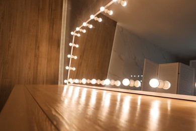 Modern mirror with light bulbs on wooden table in room, closeup