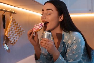 Photo of Young woman eating donut in kitchen at night. Bad habit