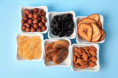 Photo of Bowls with dried fruits and nuts on light blue background, flat lay