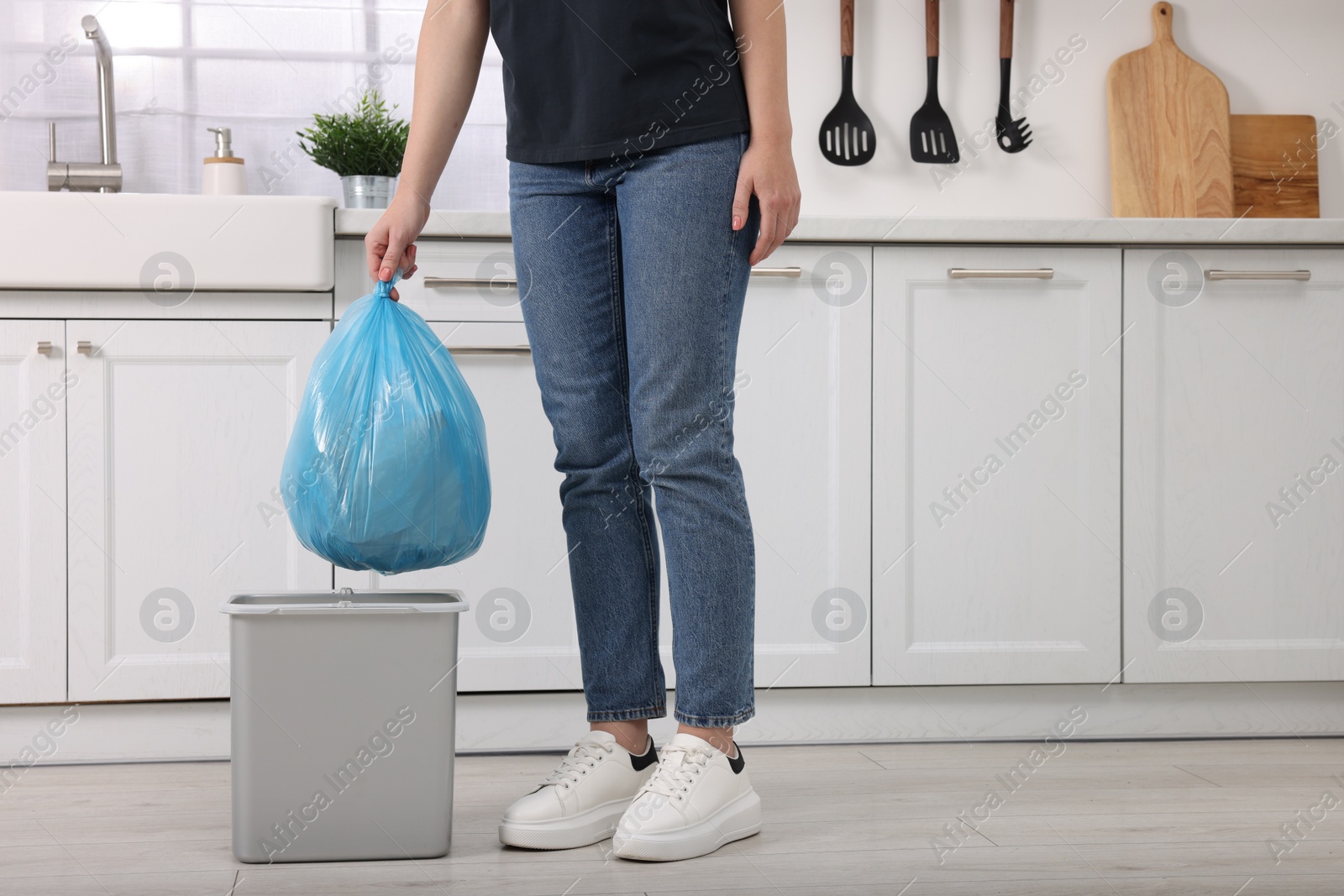 Photo of Woman taking garbage bag out of trash bin in kitchen, closeup