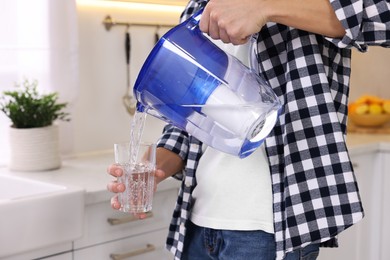 Photo of Man pouring water from filter jug into glass in kitchen, closeup