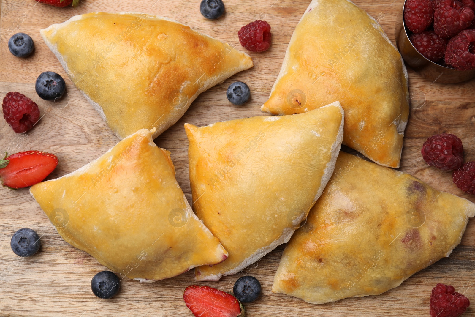 Photo of Delicious samosas and berries on wooden board, flat lay