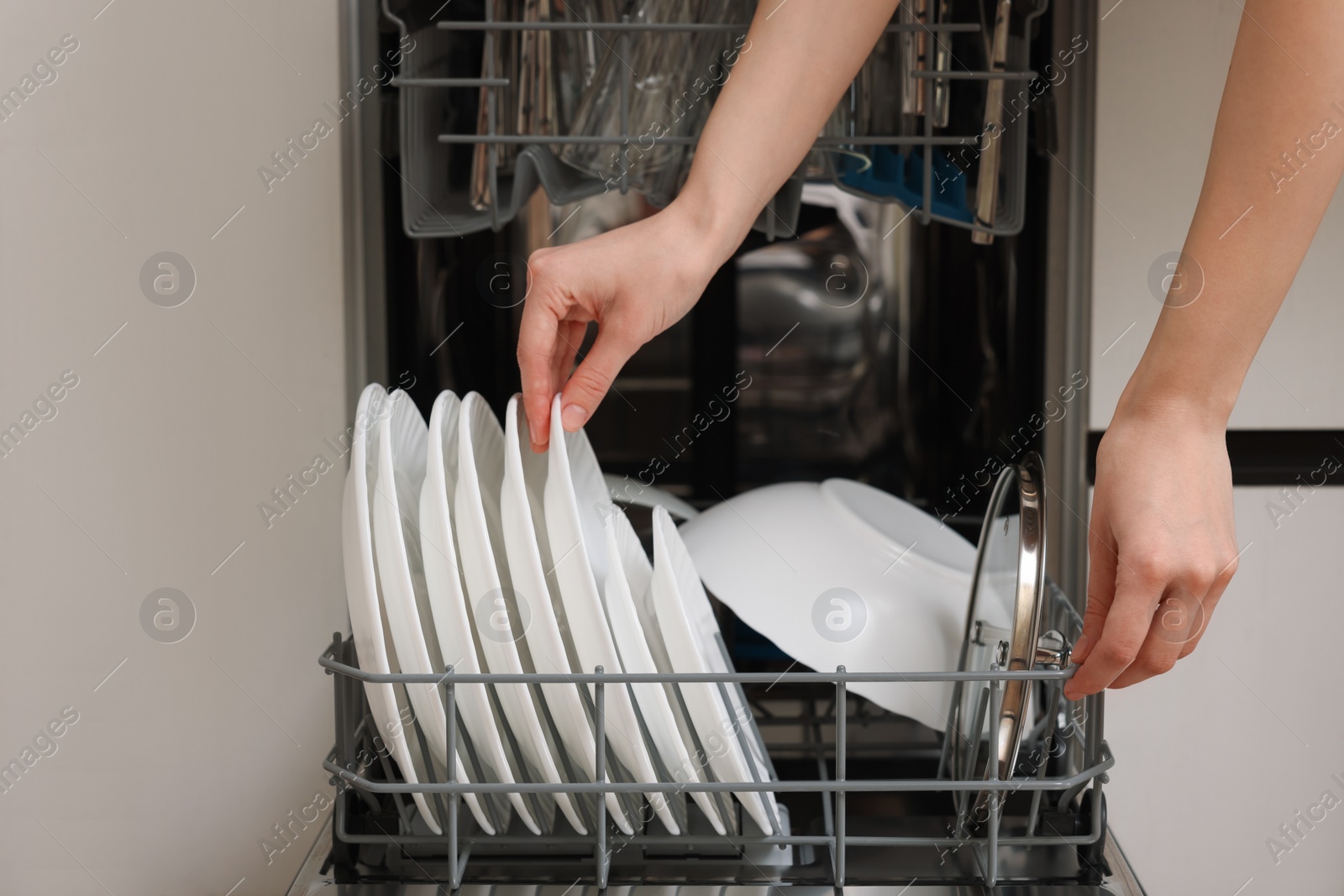 Photo of Woman loading dishwasher with plates indoors, closeup