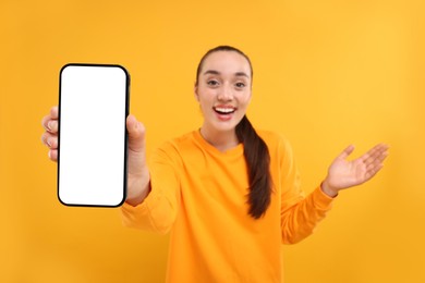 Photo of Surprised woman showing smartphone in hand on yellow background, selective focus. Mockup for design