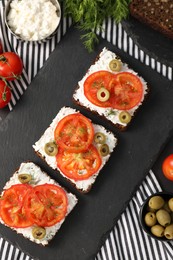 Delicious ricotta bruschettas with sliced tomatoes, olives and greens on black table, flat lay