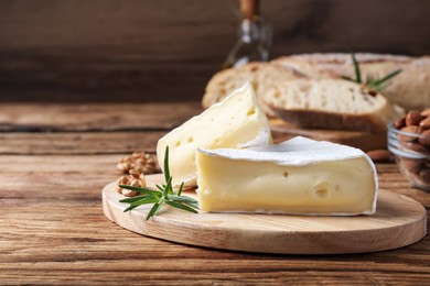 Tasty cut brie cheese with rosemary and walnut on wooden table, space for text