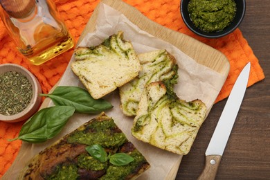 Photo of Freshly baked pesto bread with basil served on wooden table, flat lay