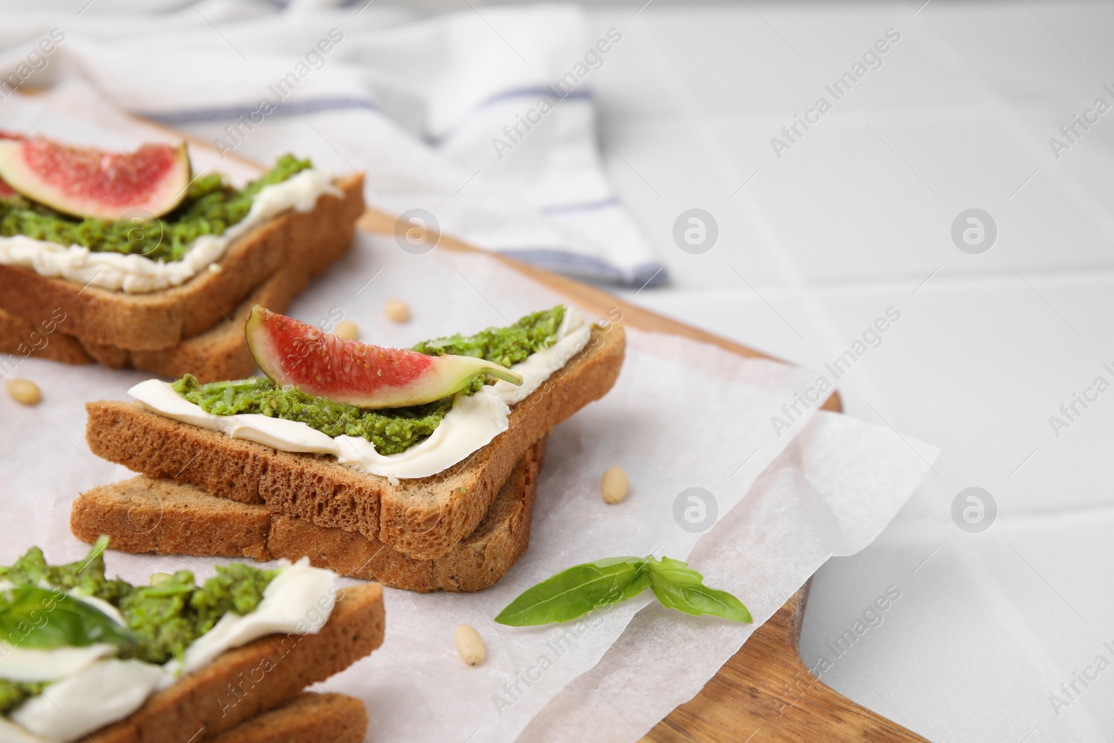 Photo of Tasty bruschetta with cream cheese, pesto sauce and fig on parchment paper, closeup