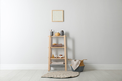 Photo of Wooden shelving unit with toiletries near white wall indoors. Bathroom interior element