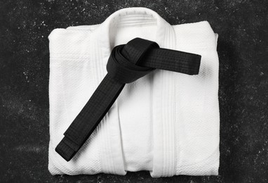 Photo of Black karate belt and white kimono on gray textured background, top view