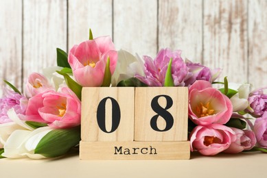 Photo of Block calendar with date 8th of March and tulips on table against wooden background. International Women's Day