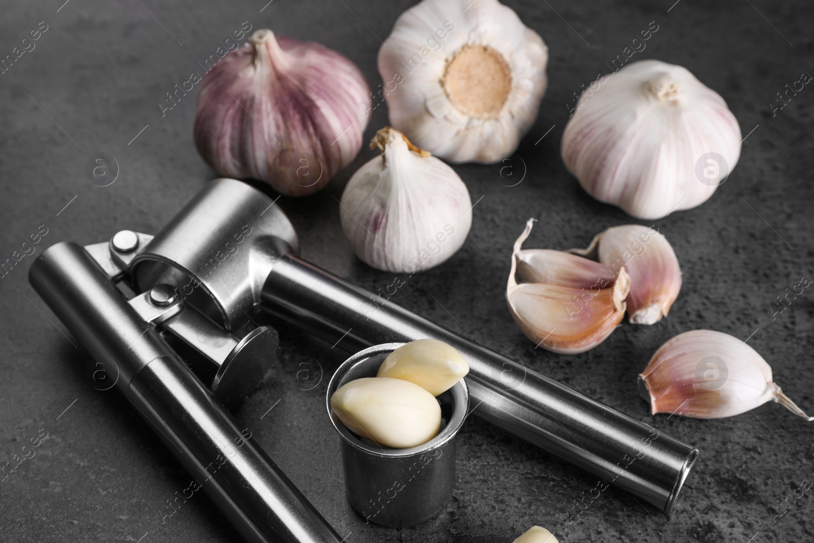 Photo of Garlic press, bulbs and cloves on grey table, closeup