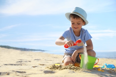 Cute little boy playing with plastic toys on sandy beach