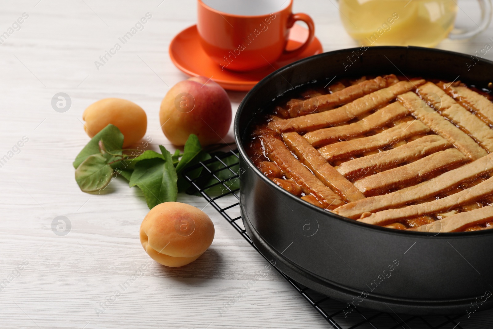 Photo of Delicious apricot pie in baking dish and fresh fruits on white wooden table, closeup