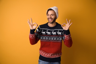 Young man in Christmas sweater and hat on yellow background