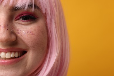 Photo of Smiling woman with bright makeup and glitter freckles on yellow background, closeup. Space for text