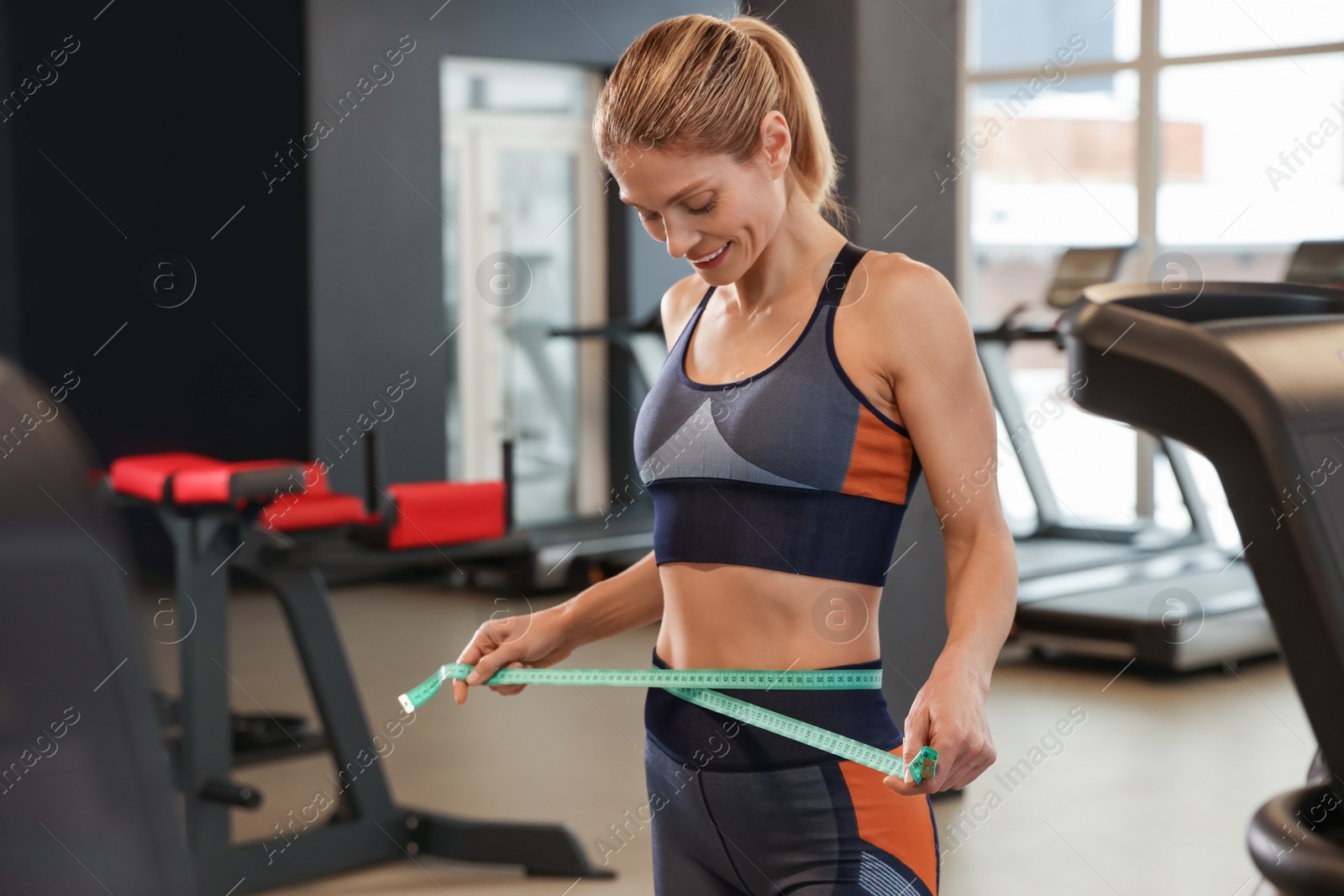 Photo of Slim woman measuring waist with tape in gym