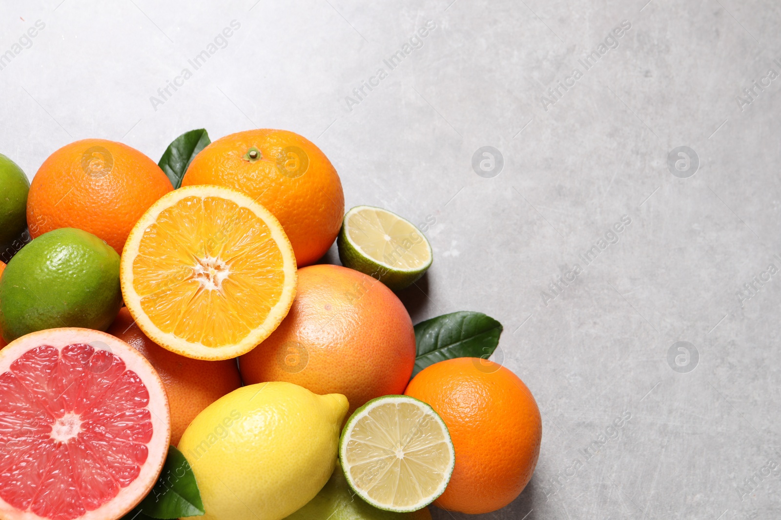 Photo of Pile of different fresh citrus fruits and leaves on grey textured table, flat lay. Space for text