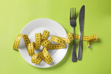 Plate, cutlery and measuring tape on green background, flat lay. Diet concept