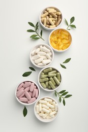 Photo of Different vitamin capsules in bowls and leaves on white background, flat lay