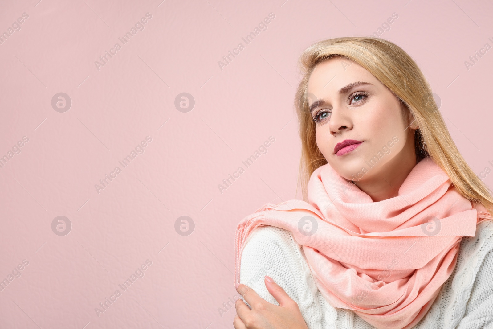 Photo of Beautiful woman wearing warm scarf on pink background, space for text. Autumn clothes