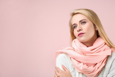 Beautiful woman wearing warm scarf on pink background, space for text. Autumn clothes