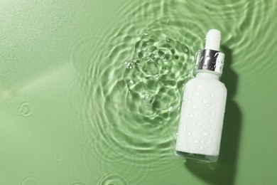 Photo of Bottle of cosmetic product in water on pale green background, top view. Space for text