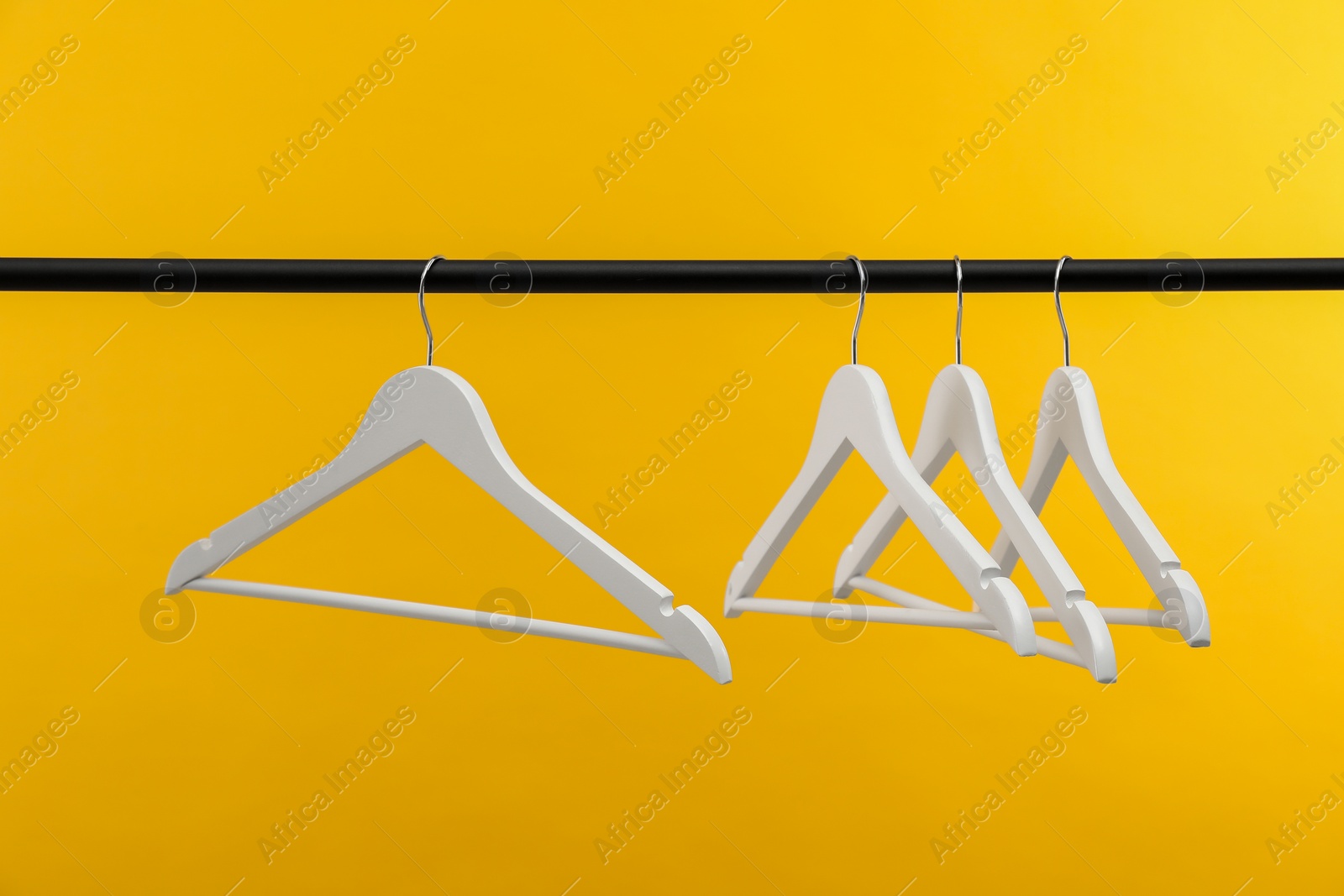 Photo of Empty clothes hangers on rack against orange background