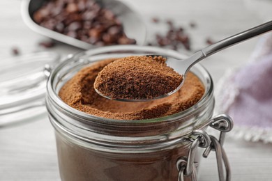 Spoon of instant coffee over jar on white table, closeup