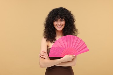 Happy woman holding hand fan on beige background