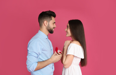 Photo of Man with engagement ring making marriage proposal to girlfriend on crimson background