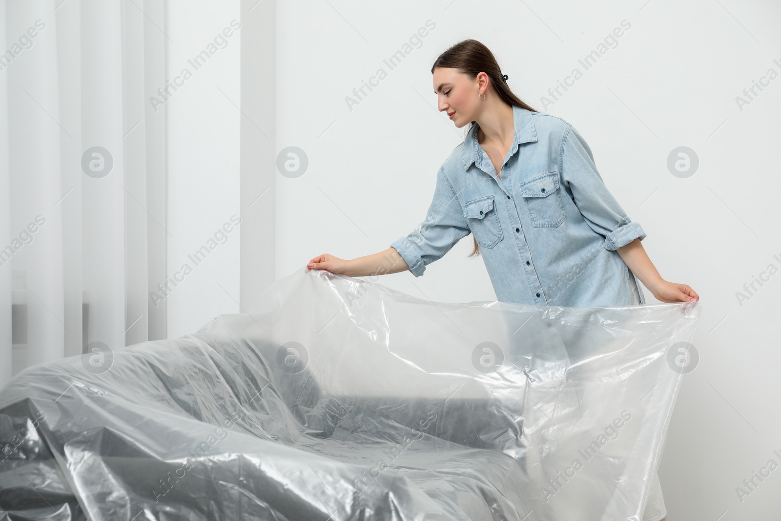 Photo of Young woman putting plastic film away from sofa at home