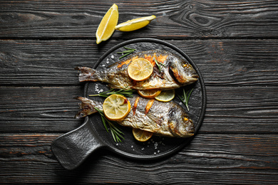 Delicious roasted fish with lemon on black wooden table, flat lay