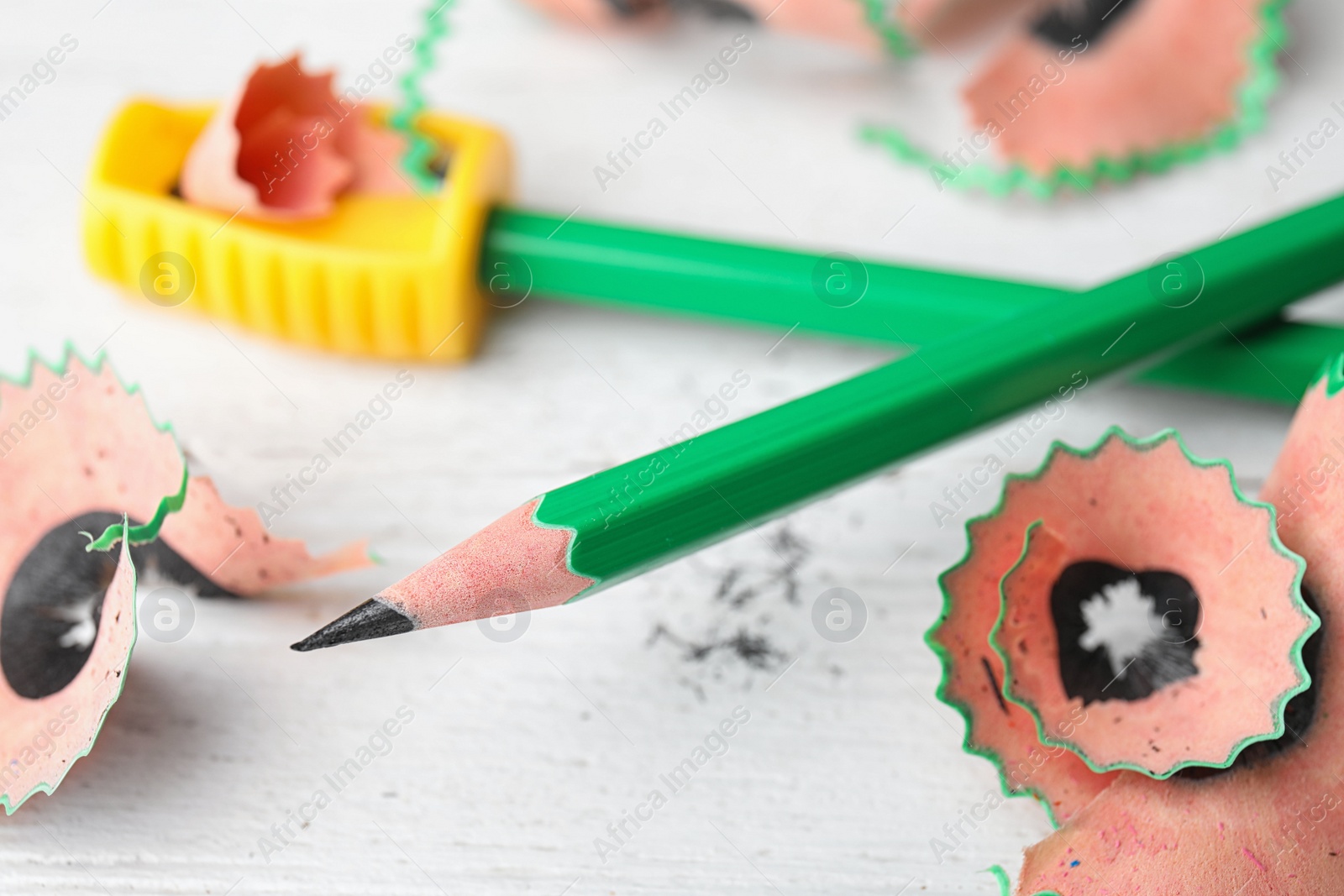 Photo of Pencils, sharpener and shavings on white table, closeup