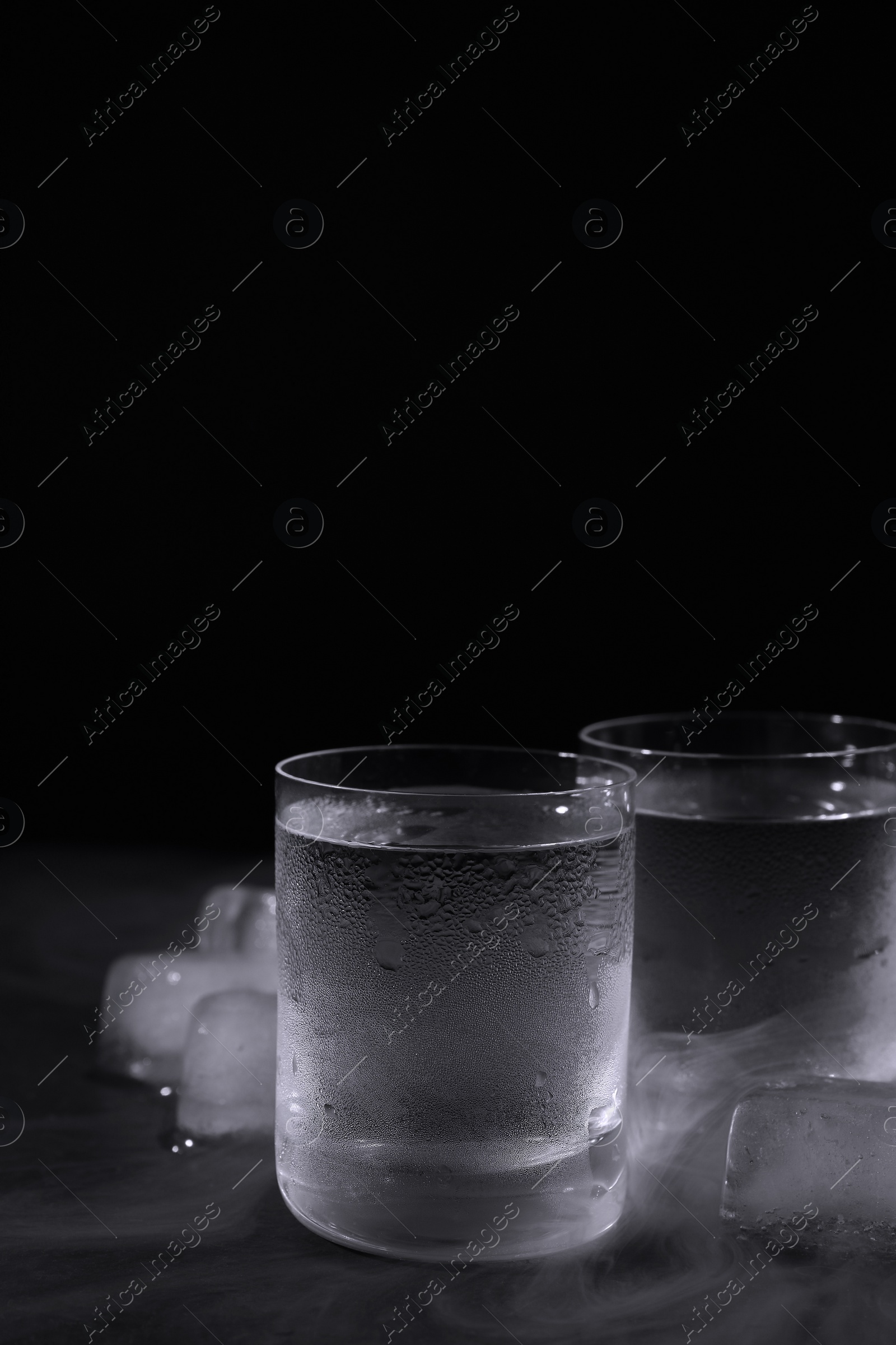 Photo of Vodka in shot glasses with ice on table against black background