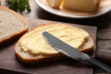 Photo of Spreading butter onto toast with knife on wooden board